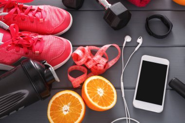 Parlak pembe koşu ayakkabıları spor ağırlıkları ve dilimlenmiş portakalların yanına oturur. Bir su şişesi, kulaklık ve akıllı telefon ahşap bir yüzeye yerleştirilir. Bu kurulum aktif bir yaşam tarzını teşvik eder.