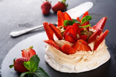 Tatlı bir tatlı siyah bir tabağa konur. Taze çilek ve nane ile kaplanmış kremalı katmanları var. Çilekler dilimlenmiş ve tatlıda düzgünce düzenlenmiş. Tabağın yanında bir bıçak var..