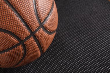 Bir basketbol topu kapalı alandaki desenli siyah bir paspasın üzerinde duruyor. Işıklandırma parlak ve topların yüzeyindeki detayları gösteriyor. Sahne, spora odaklanarak basitliği vurguluyor.