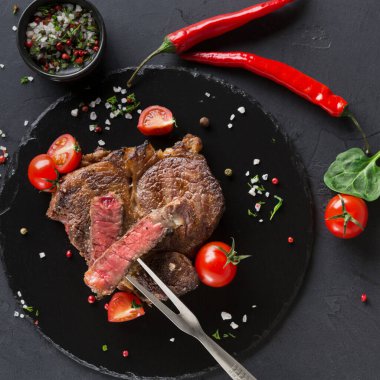 Izgara biftek siyah tabakta servis edilir. Yarım kiraz domatesli ve kırmızı biberli. Taze otlar ve tuz yakına yerleştirilir, tabağa tat katar..