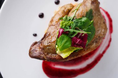 Kızarmış ördek göğsü taze yeşilliklerle süslenmiş beyaz bir tabağa yerleştirilir. Tabak, etin etrafında dairesel desenli bir böğürtlen sosuyla tamamlanıyor..