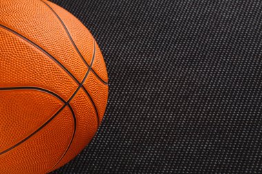 Bir basketbol topu ipliklerini ve desenlerini gösteren dokulu bir yüzeye dayanır. Bu sahne spor ekipmanlarını alıştırma veya ısınma seanslarında sıkça kullanılan bir ortamda yakalar..