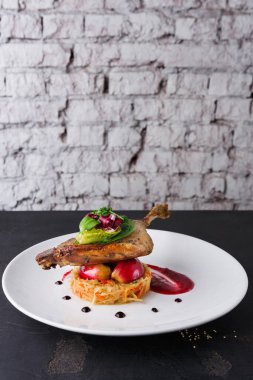 Bir tabak, pirinç tabanına yerleştirilmiş bir ördek bacağı içerir. Renkli sebzeler ve sos tabağın etrafını sarmış. Arka planda kırsal bir duvar var, yemeklerin odak noktasını arttırıyor..