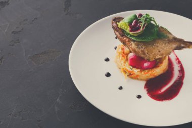 İyi hazırlanmış bir yemekte sebze tabağının tepesinde yeşillik ve renkli sosla süslenmiş bir et parçası yer alıyor. Karanlık bir yüzey ile ayarlar basit..