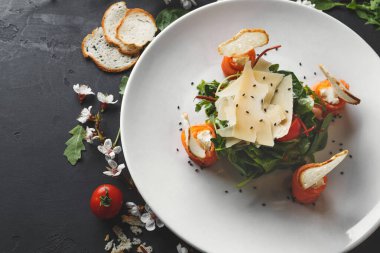 Beyaz bir tabakta taze salata, roka, somon rulosu, peynir dilimleri ve vişneli domatesler. Ekmek dilimleri ve çiçekler sahneyi süslüyor..