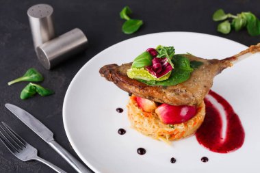 Bir tabak sebze yatağına yerleştirilmiş bir ördek bacağı içerir. Yeşilliklerle süslenmiş ve sosla eşleştirilmiştir. Masada çatal bıçak ve baharat aletleri görülebilir..