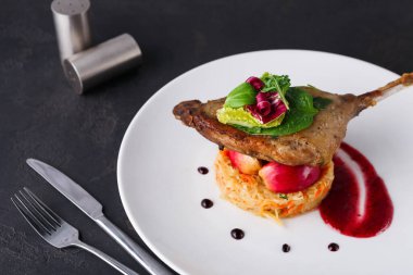 Bir sebze karışımının üzerine konmuş pişmiş ördek eti. Tabağın etrafında yeşillik ve sos var. İyi sunulmuş bir yemektir..