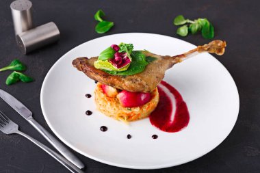 Bir ördek bacağı meyveden yapılmış bir sosun yanında pirinç tepeciğine yerleştirilir. Üstünde yeşillikler ve süslemeler var. Ayarlar basit bir yemek sahnesi gösteriyor..