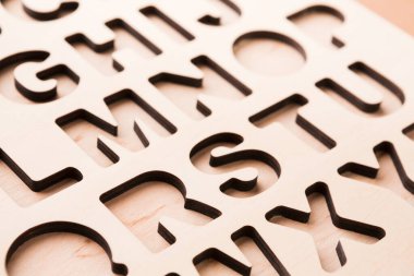 Tasarım, şebeke içinde kesilmiş harflerle düzenlenmiş düz bir tahta parçasını gösteriyor. Bu muhtemelen eğitim amaçlı ya da el işi için kullanılır. Harfler açık ve kalın..