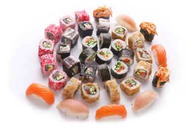 Çeşitli suşi türleri beyaz bir tabakta dairesel bir düzende sıralanır. Farklı börekler ve nigiriler var. Renkler ve şekiller çekici bir besin gösterisi yaratıyor..