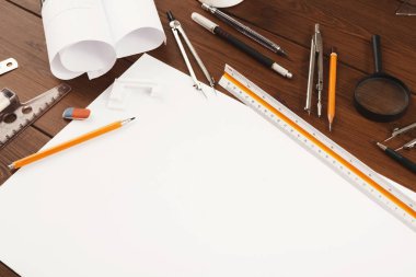 Ahşap bir masa üzerine çizim aletleri ve malzemelerin bir koleksiyonu kurulur. Ögeler arasında kağıt, kalem, cetvel ve pusulalar yer alıyor. Bu malzemeler sanatsal çalışmalar için hazır..