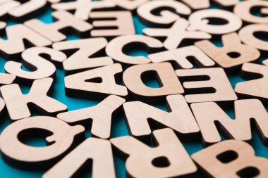 Ahşap harfler mavi arka plana saçılmış. Harflerin boyutları farklıdır ve açık renkli ahşaptan yapılmışlardır. Bu ayar öğrenme, el işi veya dekorasyon için kullanılabilir.