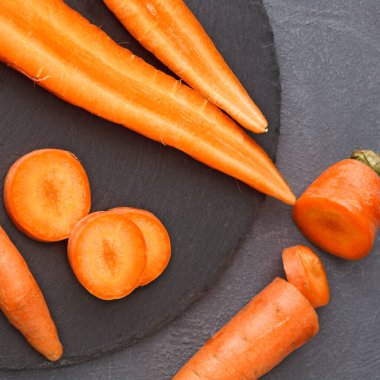 Havuçlar siyah bir taş yüzeyde düzenlenir. Bazıları bir bütün, bazıları ise mermiler halinde dilimlenmiş. Havuçların canlı turuncu renkleri ve pürüzsüz dokuları taze olduklarını gösteriyor..