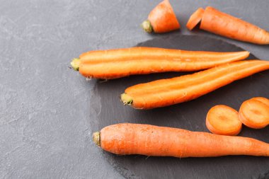 Farklı boyutlarda havuçlar koyu renkli bir taş yüzeyine yerleştirilir. Bazı havuçlar bütün iken, diğerleri yuvarlak dilimlere ayrılmıştır. Bu taze havucun doğal halini gösteriyor..