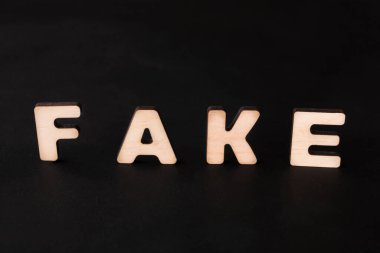 Sahte kelimesini heceleyen ahşap harfler siyah bir arkaplanda oturuyor. Harfler basit bir yazı tipinde ve gün boyunca kontrollü bir ortamda iyi ışıklandırılmış gibi görünüyor..