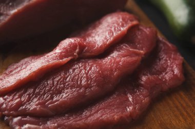 Taze kırmızı et dilimleri ahşap bir kesme tahtasına yerleştirilir. Et çiğ görünüyor ve pişirmek için hazır. Bu kurulum tipik bir mutfak hazırlık sahnesini gösteriyor.