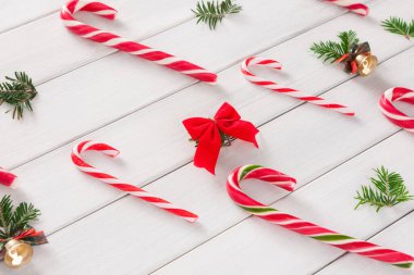 Kırmızı ve beyaz kıvrımlı şeker kamışları, çam dalları ve kırmızı bir fiyonk ile birlikte ahşap bir yüzey üzerinde yatar. Bu düzenleme mevsimlik dekorasyonlu bir tatil temasını gösterir.
