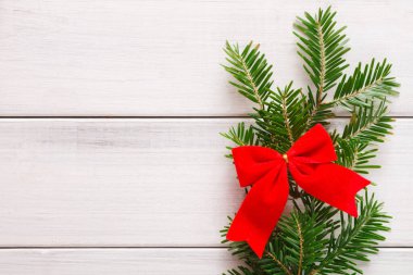 Beyaz ahşap bir yüzey üzerinde parlak kırmızı bir yay ile düzenlenmiş bir çam dalları koleksiyonu sergilenmektedir. Bu sette Noel ruhu ve toplantılar için şenlikli dekorasyon fikirleri sergileniyor..