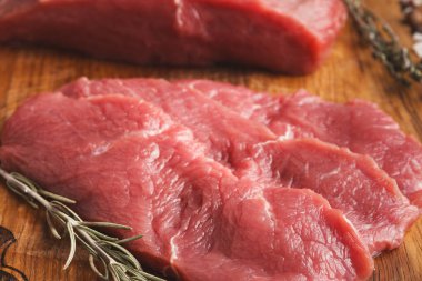 Çiğ sığır eti kesikleri tahta bir tahtanın üzerinde sergilenir. Bazı kesikler ince, diğerleri daha kalın. Taze otlar etin yanına konur, mutfakta pişirilmeye ya da hazırlanmaya hazırdır..