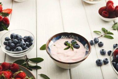 Taze böğürtlenler ahşap bir masada bir kase yoğurdun etrafına konur. Yabanmersini, çilek ve ahududu küçük kaselerde düzenlenir. Ayarlar yaz yemeği hazırlıklarını gösteriyor..
