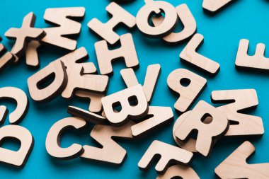 Resim, parlak mavi bir yüzeye dağılmış çeşitli ahşap harfleri gösteriyor. Bu mektuplar eğitim amaçlı ve el işi projeleri için kullanılabilir. Tasarımda sade ve basitler..