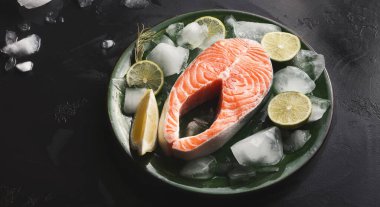 Somon filetosu buzla çevrili yeşil bir tabağa konur ve siyah bir yüzeye limon dilimleri konur. Bu düzen mutfakta yemek hazırlamak için tipik bir yöntemdir..