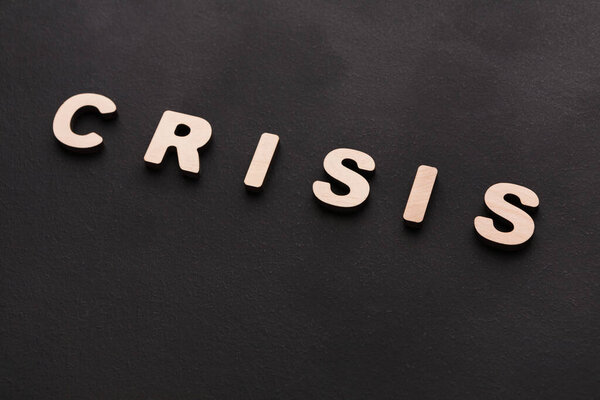 Wooden letters are arranged to spell crisis on a dark background. The setting shows a focus on the word. The scene captures a single message in a clear layout.