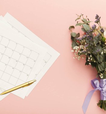 Pembe bir yüzeye bir takvim örtüsü yerleştirilir. Onun yanında, kurdeleli bir buket var. Takvim kağıtlarının üzerine bir kalem yerleştirildi.