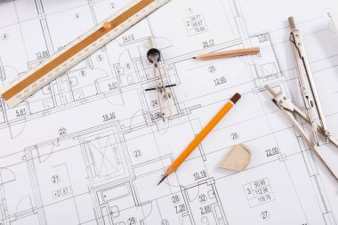 Mimari planların üzerine bir set taslak araçları düzenlenir. Çalışma alanı bir cetvel, pusula, kalem ve bir terazi içerir. Bu ögeler inşaat veya tasarım işleri için kullanılır..