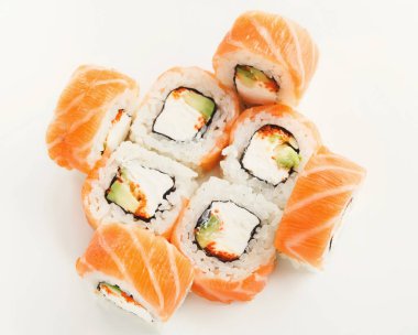 Beyaz arka planda bir somon suşi rulosu koleksiyonu var. Suşide somon tabakaları var ve içinde avokado ve krem peynir var. Her rulo parçalara ayrılıp düzenlenir..