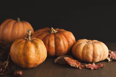 Farklı boyutlarda birkaç balkabağı sonbahar yapraklarıyla çevrili ahşap bir masanın üzerine yerleştirilir. Koyu arkaplan balkabaklarını ve dokularını ön plana çıkarıyor..