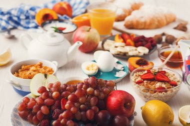 Kahvaltı yiyecekleri bir masanın üzerinde düzenlenir. Yayılımda çeşitli meyveler, tahıllar, kruvasanlar ve içecekler yer alıyor, parlak ve davetkar bir sabah yemeği gösterisi sergileniyor..