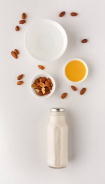 Beyaz bir yüzeye çeşitli yiyecek parçaları yerleştirilir. Badem yağı ve badem yağıyla çevrili bir cam şişe badem sütü ortada duruyor. Bu kurulum sağlıklı yeme seçeneklerini teşvik ediyor..