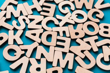 Sahne, mavi arka plana yayılmış ahşap harfleri gösteriyor. Harfler farklı yönlerde ve neşeli bir atmosfer yaratıyor. Bu düzenleme öğrenme ve oyunlar için kullanılabilir.