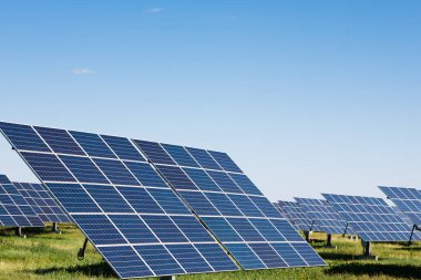 Güneş panelleri büyük bir alanda dizilmiştir. Güneş ışığını yakalamak için konumlandırıldılar. Gökyüzü mavi ve berrak. Bu ayar güneş enerjisi kullanan kırsal bölgelerde yaygındır..