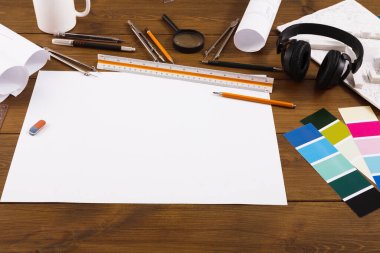 Çeşitli eşyalardan oluşan bir kolaj ahşap bir masaya yayılır. Kalemler, cetveller, renk örnekleri ve çizim ya da tasarım için hazır boş kağıtlar var. Kulaklıklar yakınlarda, işe odaklanmamızı öneriyorlar..