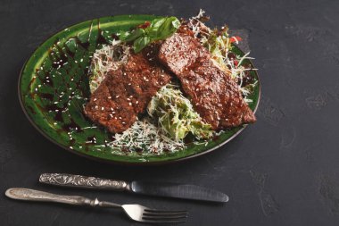 Bir tabakta gevrek salata yatağına yerleştirilmiş lezzetli biftekler var. Taze otlar ve bir tutam sos tat katar. Sofra kurulumunda yemek için çatal bıçak var..