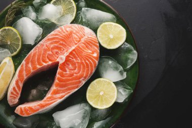 Birçok somon filetosu taze limon dilimleriyle çevrili bir buz yatağında oturur. Sahne karanlık bir mutfak tezgahında geçiyor. Bu yiyecek düzenlemesi balıkların hazırlanmasını vurguluyor.