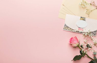 Bir kolajda pembe arka planda çiçekler ve kırtasiye parçaları sergileniyor. Çiçekler arasında bir gül ve küçük beyaz çiçekler vardır. Zarf dekoratif unsurlar içeriyor.