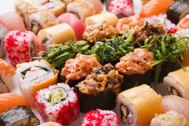 Beyaz arka planda bir suşi rulosu koleksiyonu sergilenir. Balık, sebze ve pirinç dahil olmak üzere çeşitli suşi türleri gösterilir. Her rulo eşsiz malzeme ve renklere sahiptir..