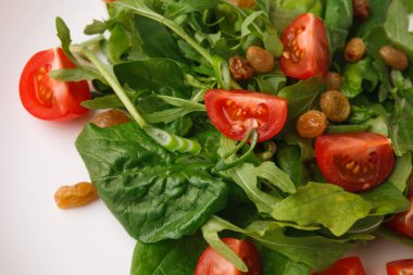 Bir kase roka ve ıspanaktan yapılmış taze salata içerir. Çeri domatesleri ve kuru üzümler yeşilliklere karıştırılır. Salata beyaz bir tabakta ve davetkar görünüyor..