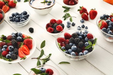 A collection of various berries including strawberries, blueberries, raspberries, and blackberries is displayed in clear bowls.