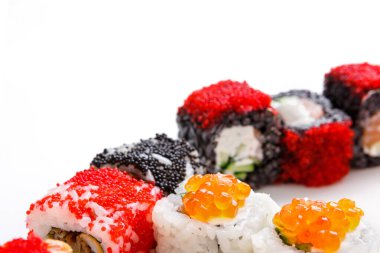 Farklı suşi ruloları beyaz bir tabakta düzenlenir. Rulolarda kırmızı ve siyah balık yumurtası da dahil olmak üzere çeşitli malzemeler yer alıyor..