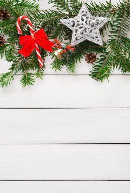 Bayram eşyalarından oluşan bir kolaj gümüş bir yıldız, kırmızı ve beyaz bir baston şeker ve yeşil çam ağaçlarına yerleştirilmiş küçük kozalakları gösteriyor. Bu süslemeler basit beyaz tahta bir masa üzerinde düzenlenmiştir..