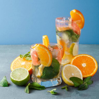İçeceklerle dolu iki bardak masaya oturur. İçeceklerde portakal, limon ve nane yaprakları var. Taze meyve bardakların etrafına saçılmış..