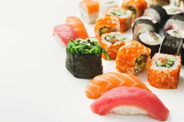 Beyaz arka planda birden fazla çeşit suşi düzenlenir. Tabakta nigiri, maki dürümleri ve diğer suşi seçenekleri yer alıyor. Her parçada farklı malzemeler ve malzemeler var..