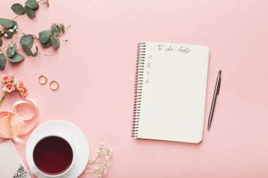 Açık pembe arkaplana bir takım nesneler yerleştirilir. Bir fincan çay, yapılacaklar listesi olan bir not defteri ve dekoratif çiçekler var. Düzenlemeye kalem ve yüzükler de dahildir.