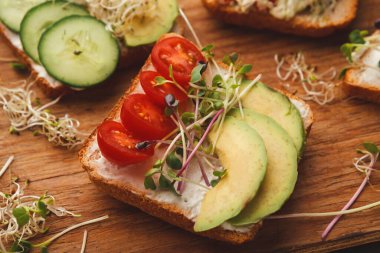 Taze sebzelerle kaplı dilimlenmiş ekmek kolajı. Düzenleme salatalık, domates, avokado ve filizleri içeriyor. Ev mutfağında ahşap bir yüzeye kurulmuş..