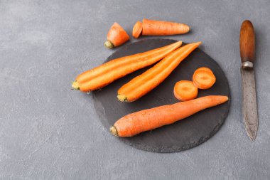 Taze havuçlar siyah bir kesme tahtasına konur. Bazı havuçlar bir bütün, diğerleri ise yuvarlak parçalara bölünmüş. Yemek hazırlamak için havucun yanına bir bıçak yerleştirilir..