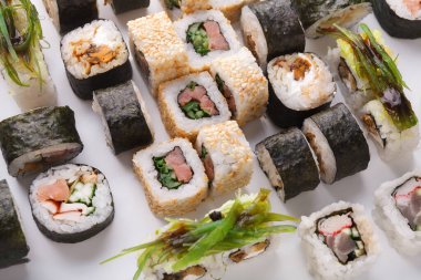 Farklı suşi ruloları beyaz bir tabakta düzenlenir. Koleksiyonda pirinç, deniz yosunu ve sebze gibi çeşitli malzemeler yer alıyor. Bu vitrinlerde çeşitli suşi türleri ve hazırlıklar var..